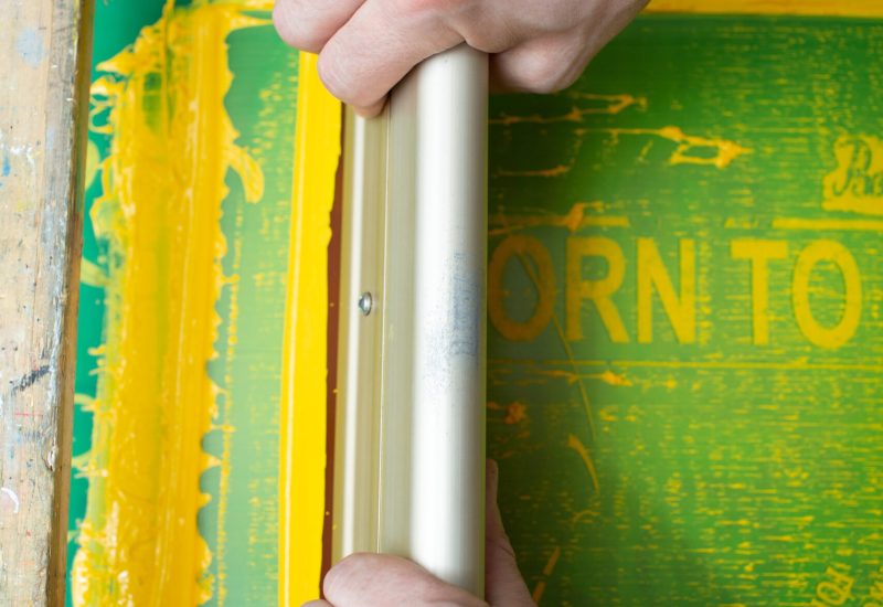 Serigraphy silk screen print process at clothes factory. Frame, squeegee and plastisol color paints.
